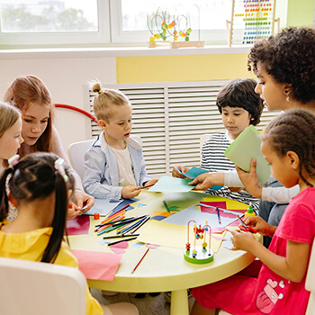 Student teachers work with children on a project around a table.