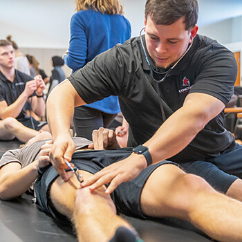 Male student practices listening to blood flow on another student’s leg.