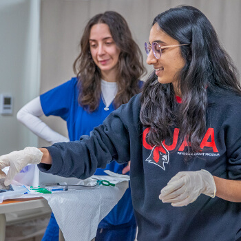 A female student practices catheterization on a manikin in a simulated hospital room.